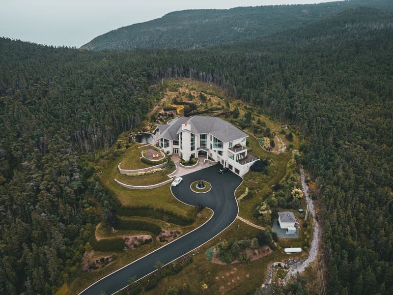 Aerial drone view of a modern home set on a forested hill by the sea