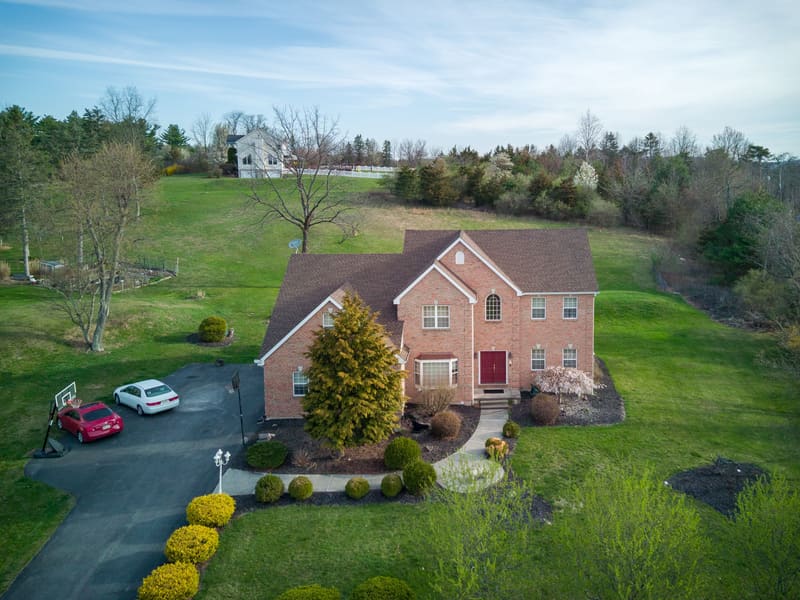 Vue aérienne par drone d'une maison en brique montrant l'entrée, le terrain et les arbres matures